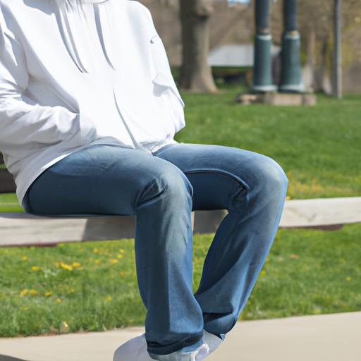 Người mặc quần jean ống rộng màu sáng và áo hoodie trắng, ngồi trên ghế đá trong công viên.